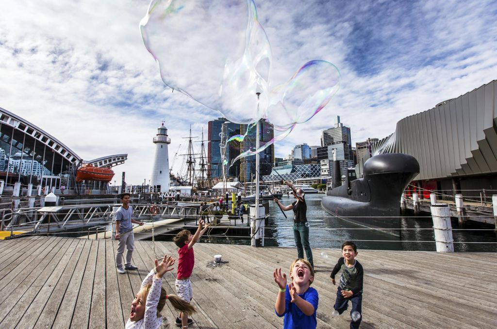 잠수함과 도시 풍경을 배경으로 물가 선착장에서 커다란 비눗방울을 가지고 노는 어린이들.