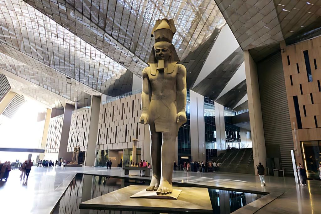 반사되는 표면과 높은 천장이 있는 현대적이고 넓은 내부에 고대 이집트 인물의 커다란 조각상이 있습니다.