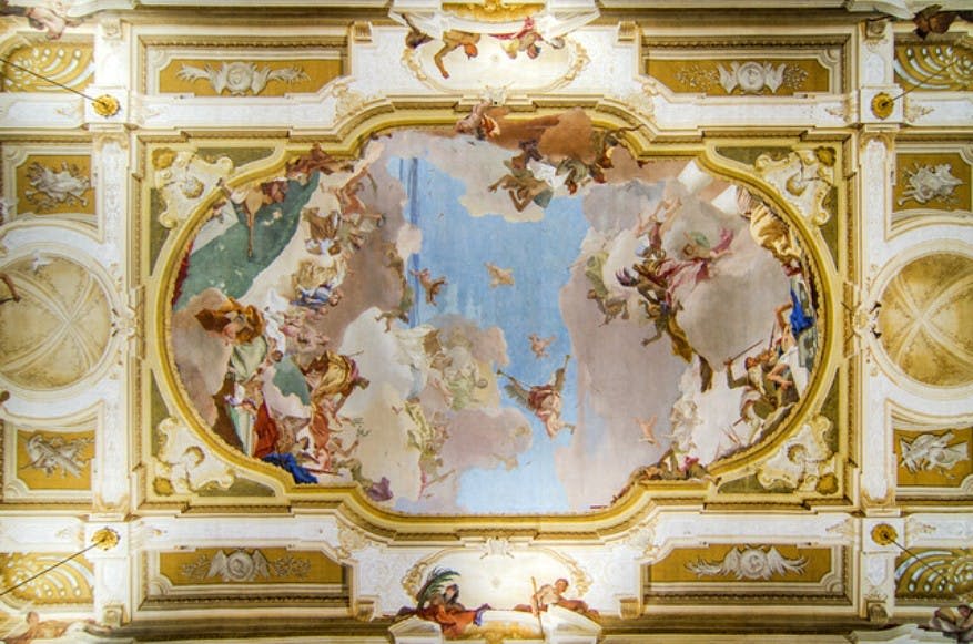 정교한 금색과 흰색 건축 디테일로 둘러싸인 형상과 구름이 특징인 바로크 양식의 천장 프레스코화.