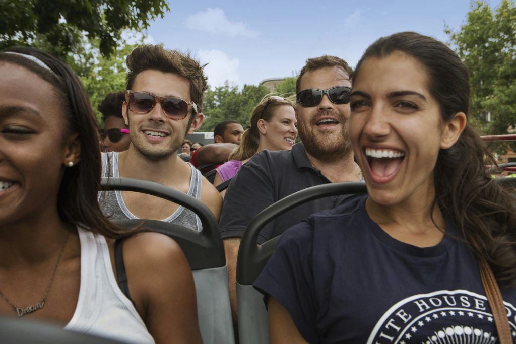 선글라스와 캐주얼한 옷을 입고 나무를 배경으로 버스나 셔틀을 타며 미소를 짓는 어른들.