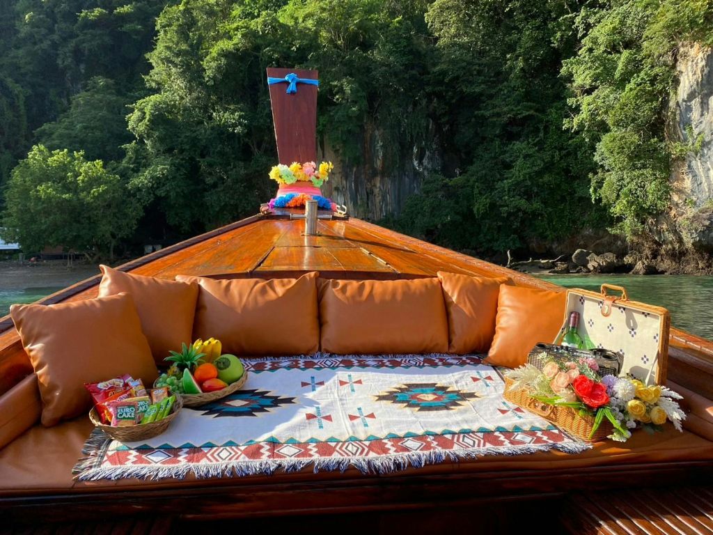 푸르른 나무를 배경으로 갈색 쿠션으로 둘러싸인 보트 데크의 장식된 담요에서 과일과 간식을 즐겨보세요.