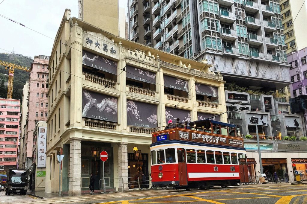 빈티지한 빨간색과 흰색 트램이 더 폰 (The Pawn) 이라는 유서 깊은 건물 앞을 지나고 있으며, 현대적인 도시 건물이 배경으로 자리하고 있습니다.