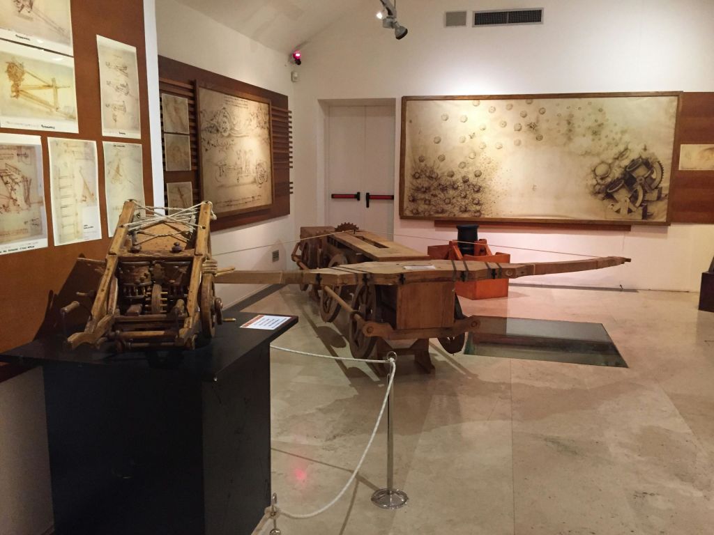 흰색 로프 장벽으로 분리된 벽에 목재 기계 모델과 대형 세피아 도면으로 채워진 객실.