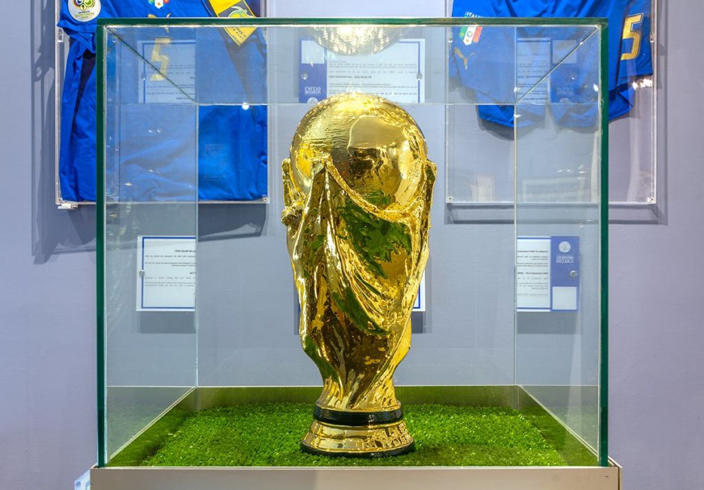 푸른색 스포츠 유니폼을 배경으로 초록색 잔디가 패치된 유리 케이스에 표시된 황금색 트로피입니다.
