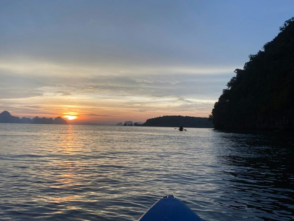 화려한 하늘을 배경으로 카약과 해안선의 먼 실루엣을 감상하며 석양에 고요한 바다에서 카약을 즐겨보세요.