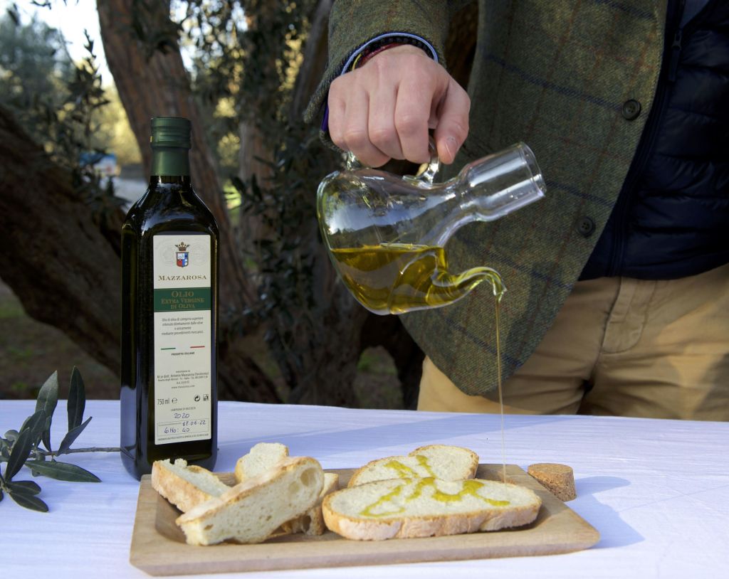 유리병에 담긴 올리브유를 나무판에 썬 빵에 붓고 올리브유 한 병을 곁들인 사람.