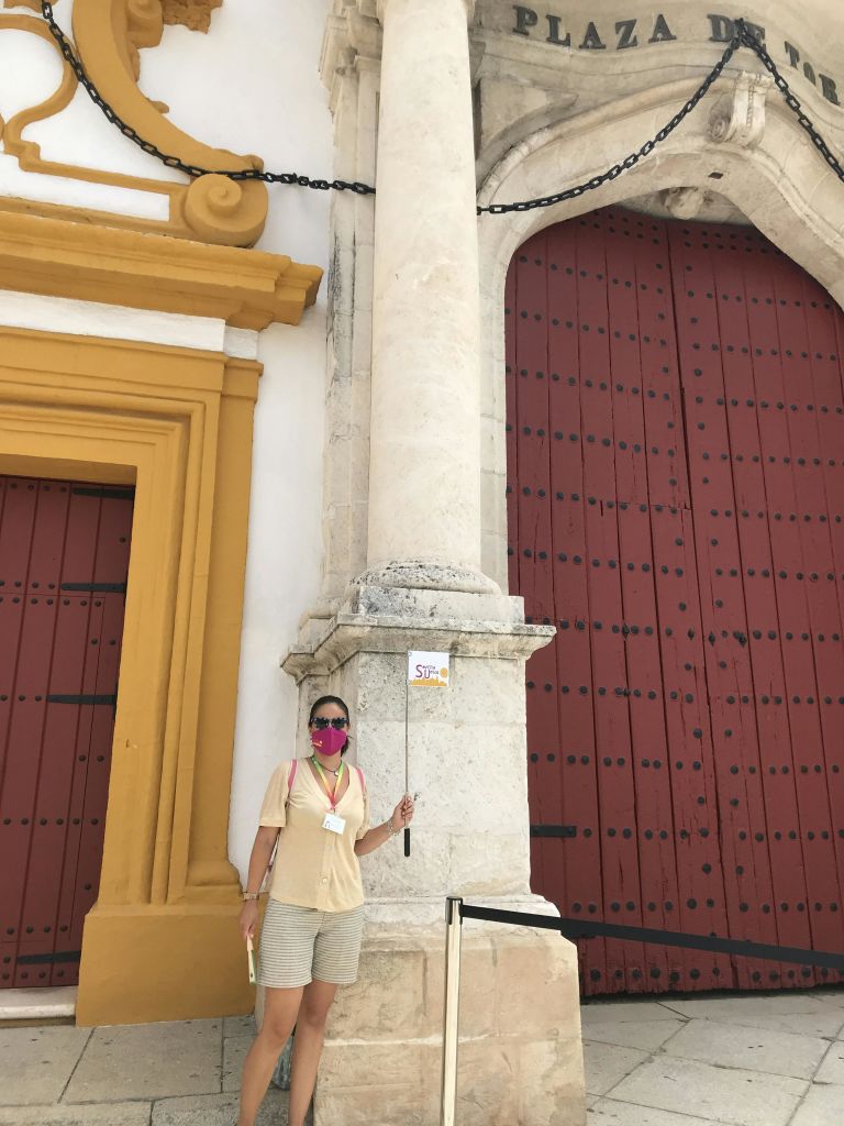 마스크를 착용한 사람이 빨간색과 노란색으로 표시된 커다란 문 근처에 서서 'STOP' 이라고 적힌 팻말을 들고 있습니다.