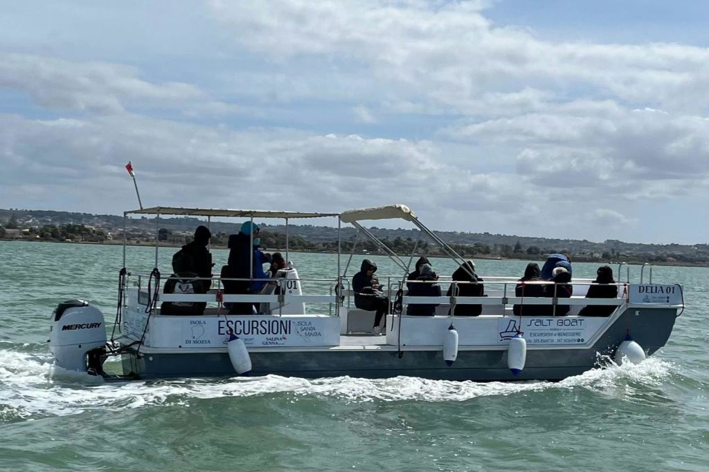 부분적으로 흐린 하늘 아래 물 위에 "Escursioni" 라고 표시된 작은 투어 보트에 앉은 한 무리의 사람들.