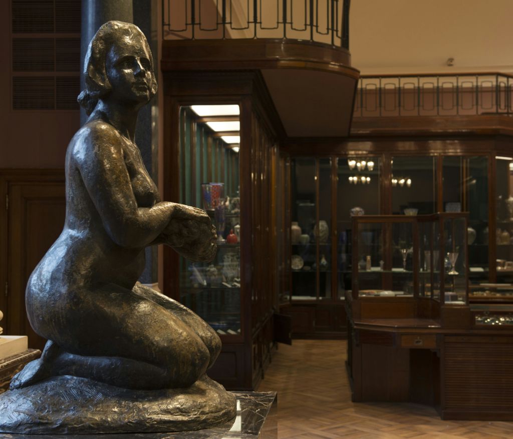 유리 진열 케이스와 나무 바닥이 있는 조명이 희미한 박물관 방에서 무릎을 꿇은 청동 동상.