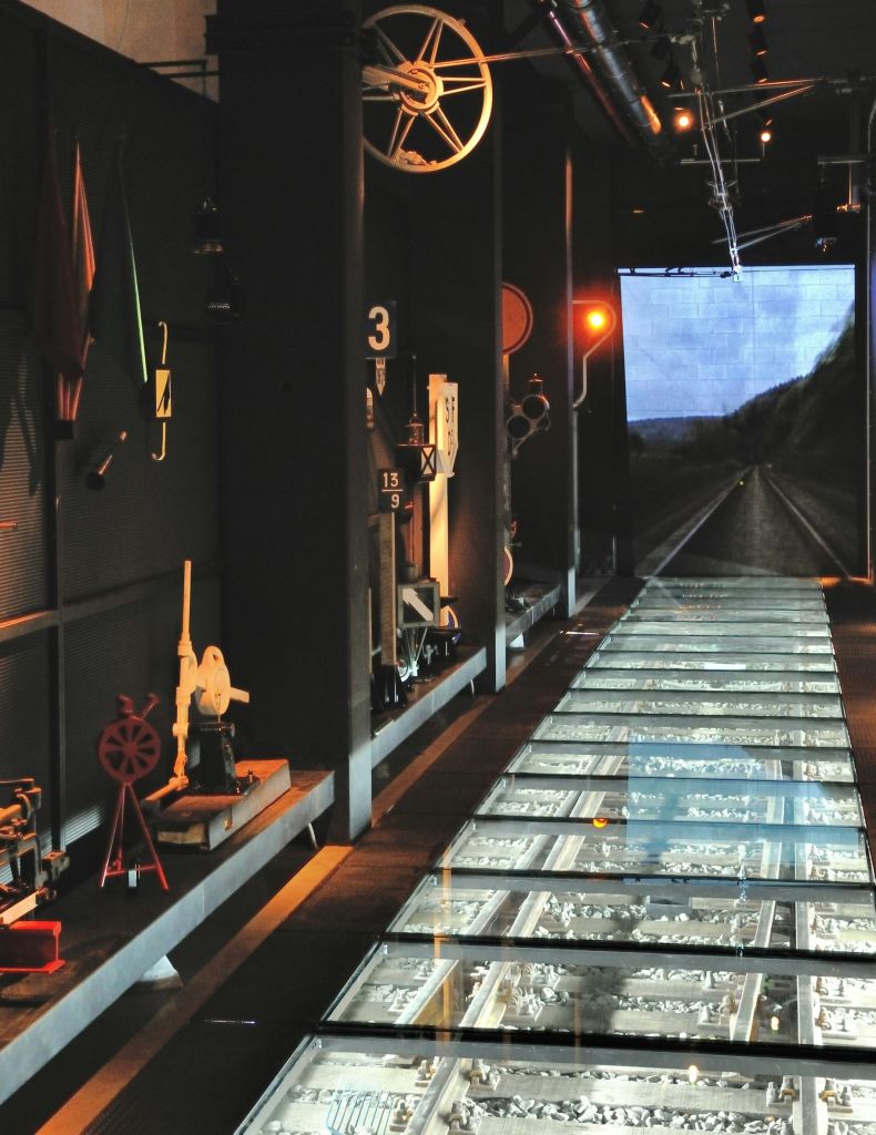 빈티지 철도 장비와 철로가 보이는 유리 바닥이 특징인 박물관 전시관은 철도의 비디오 화면으로 이어집니다.