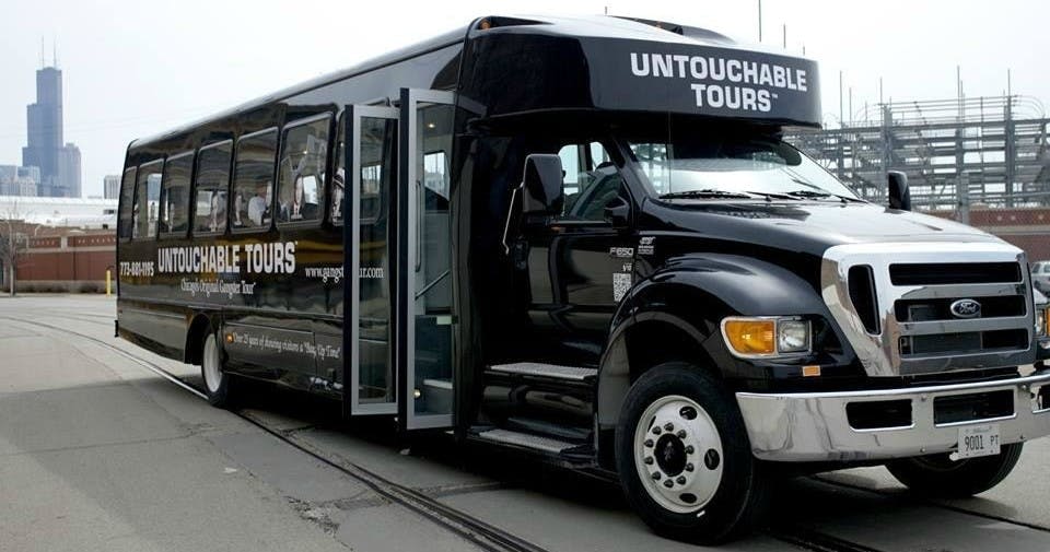 "Untouchable Tours" 라고 표시된 검은색 투어 버스가 문을 열고 주차되어 있으며 내부의 일부를 보여줍니다.