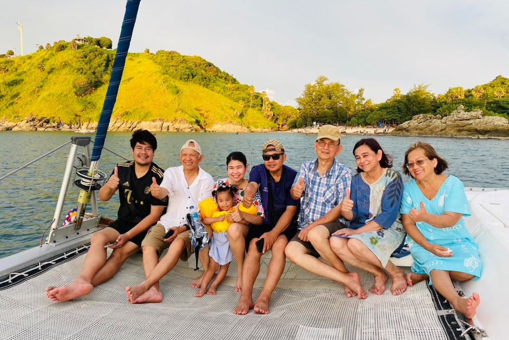 어린이를 포함한 6명이 보트에 앉아 푸른 언덕을 배경으로 아름다운 풍경을 감상하며 모두 엄지손가락을 치켜들고 미소를 짓고 있습니다.