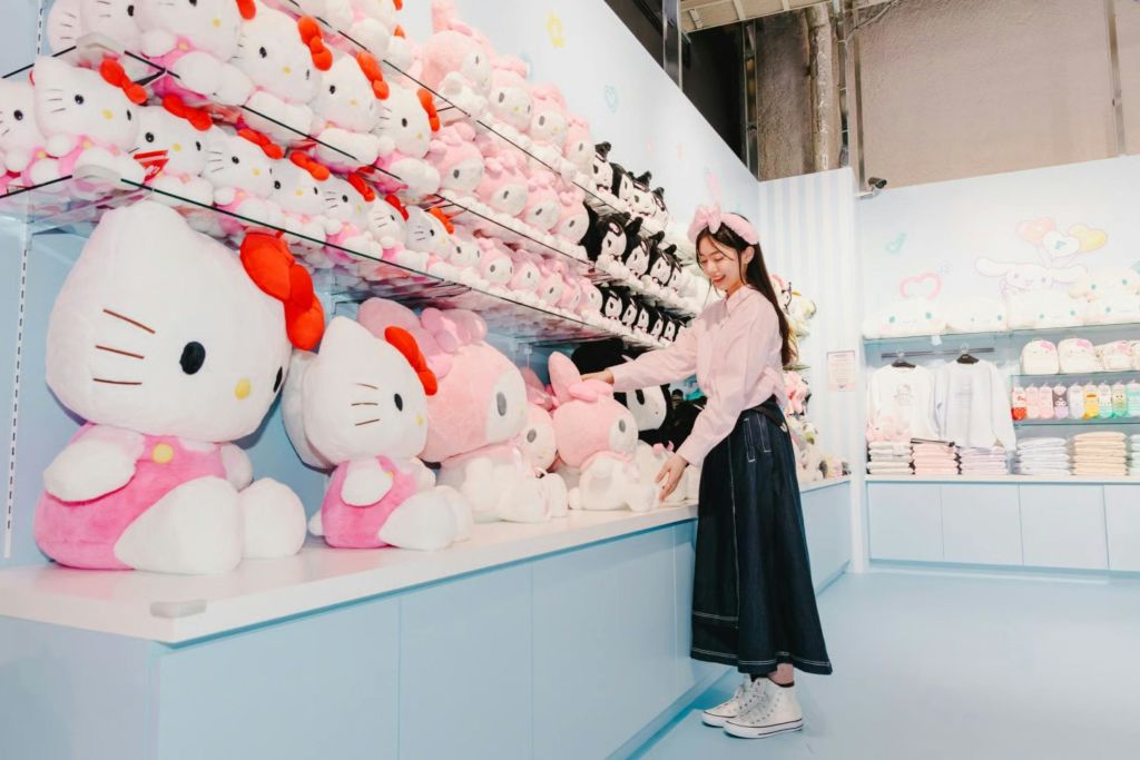 한 사람이 파스텔 테마의 매장에 서서 선반 위에 놓인 고급 장난감에 둘러싸여 상호 작용하면서 미소를 짓고 있습니다.