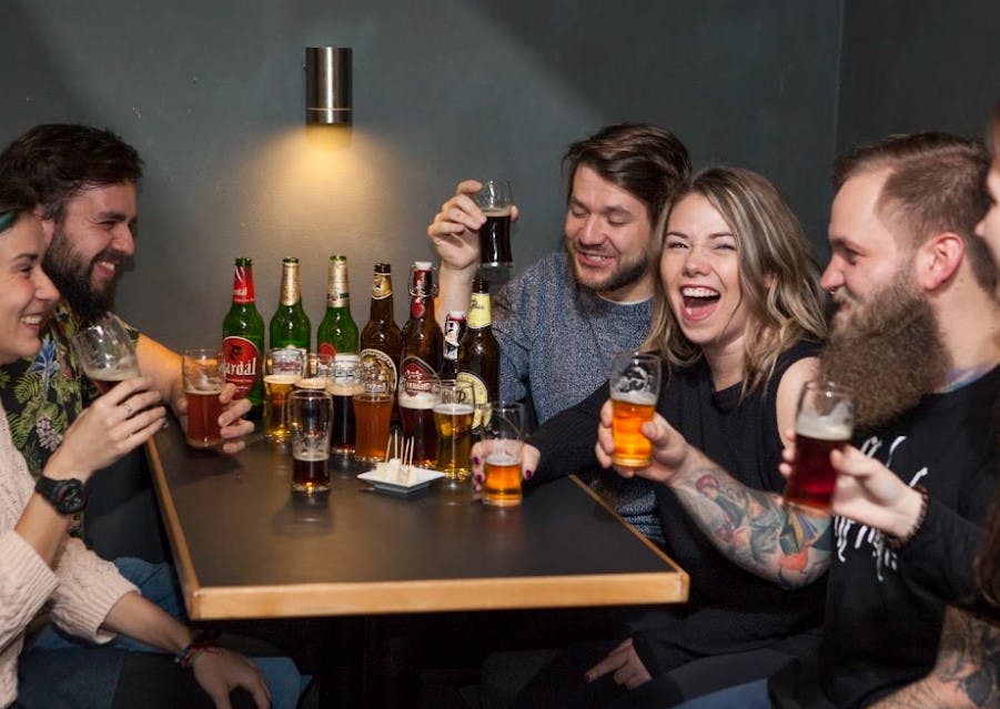 다양한 맥주병과 잔이 놓인 테이블에서 웃으며 맥주잔을 들고 있는 친구들.