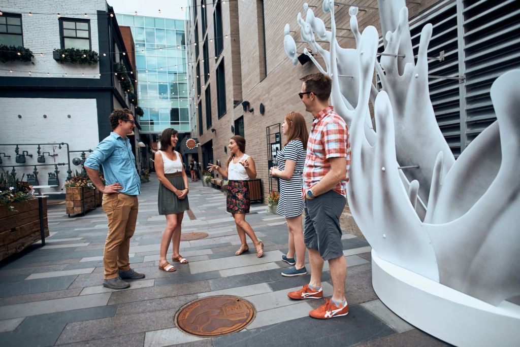 주변에 장식 예술품, 식물, 건물이 있는 현대적인 야외 도시 공간에서 다섯 명이 이야기를 나누고 있습니다.