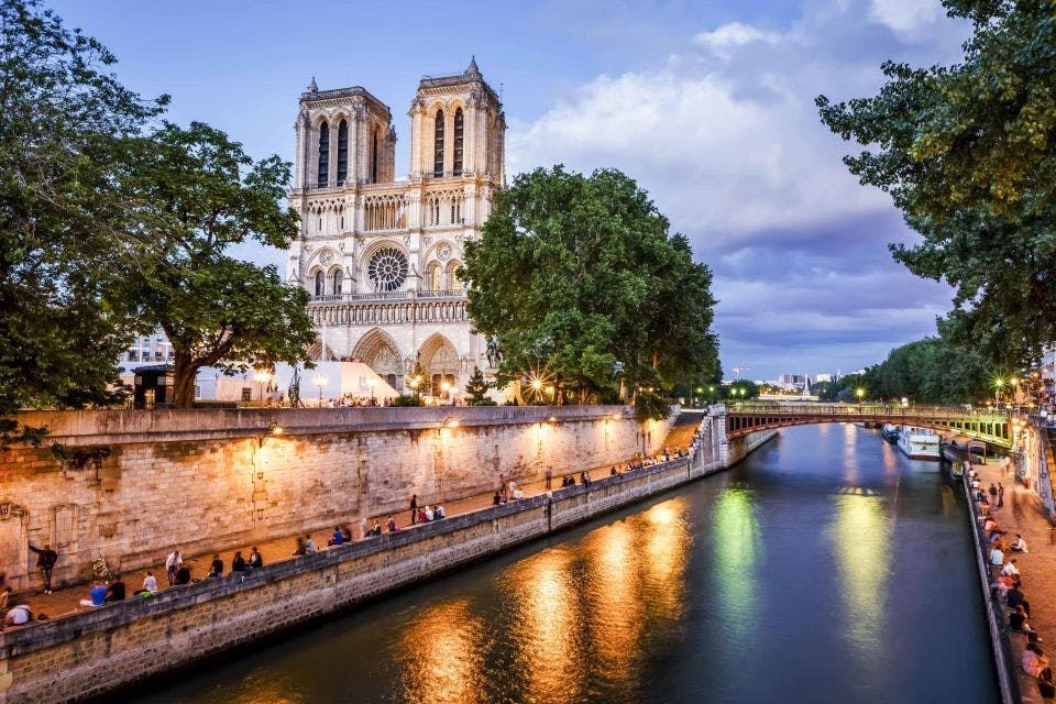 해질 무렵의 노트르담 대성당에는 센강의 조명이 비추고 강변 길을 따라 걷는 사람들이 있습니다.