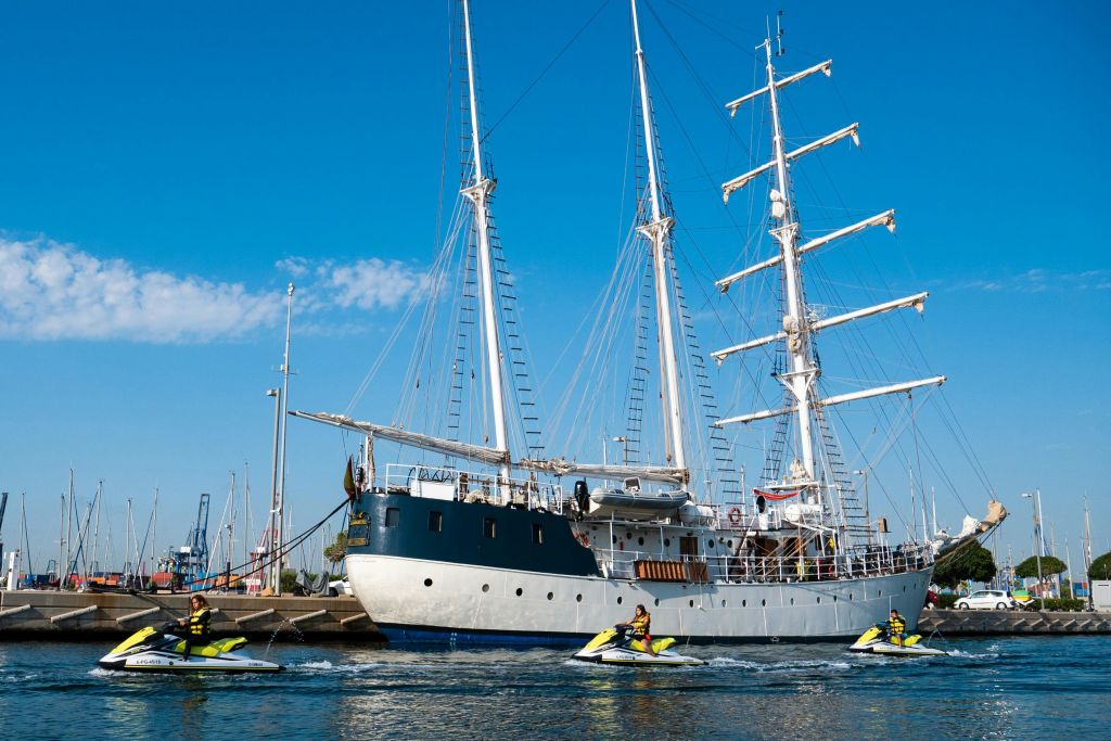 화창한 날 두 척의 대형 범선이 나란히 정박했습니다. 보트 근처에서 제트 스키를 타는 사람들.