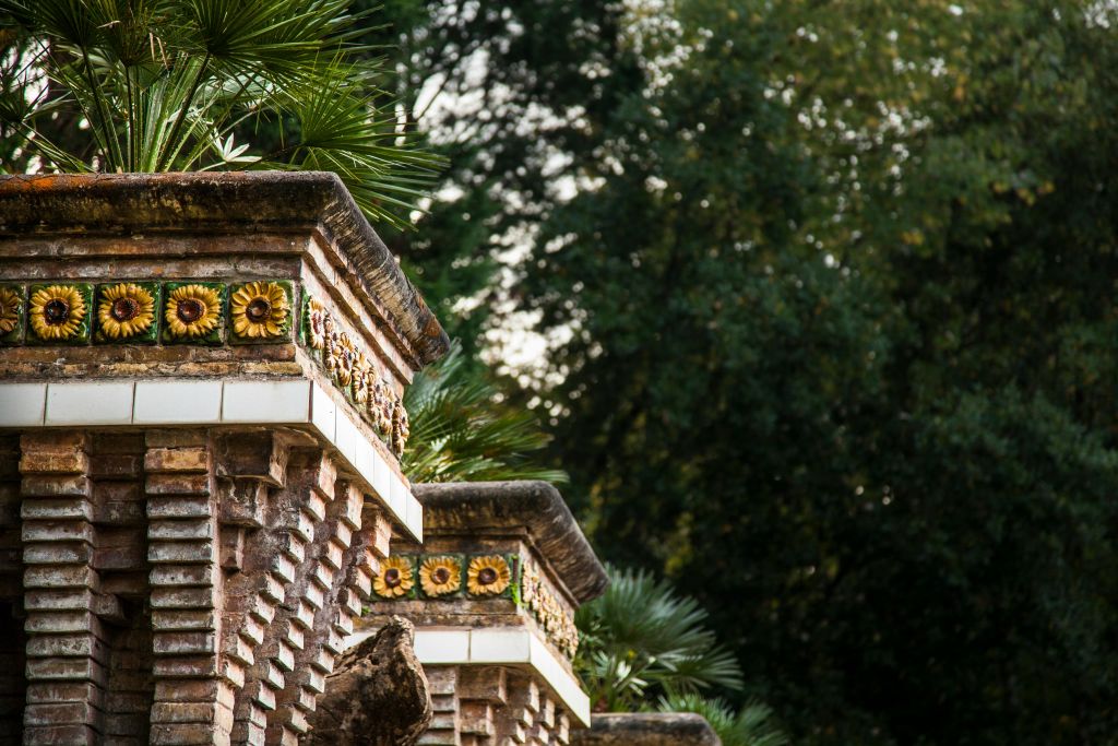 해바라기 타일로 장식된 벽돌 구조는 울창한 녹지로 둘러싸여 있으며, 그 꼭대기에는 야자수 프론드가 보입니다.