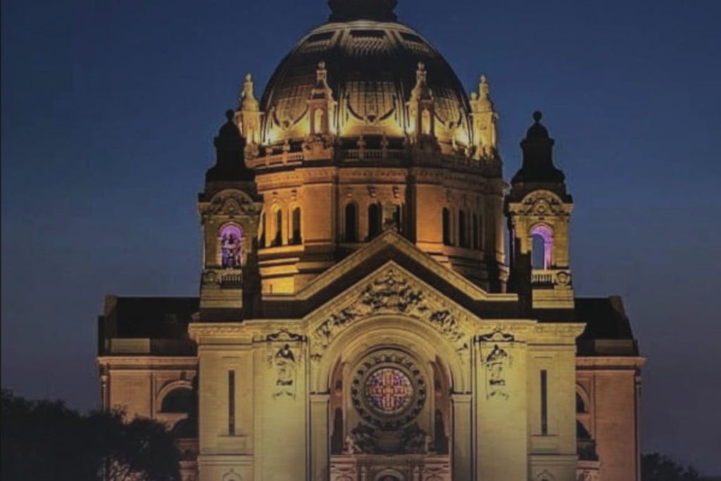 정교한 건축 디테일과 스테인드글라스 창문이 특징인 야간 조명으로 장식된 대성당 돔과 외관.