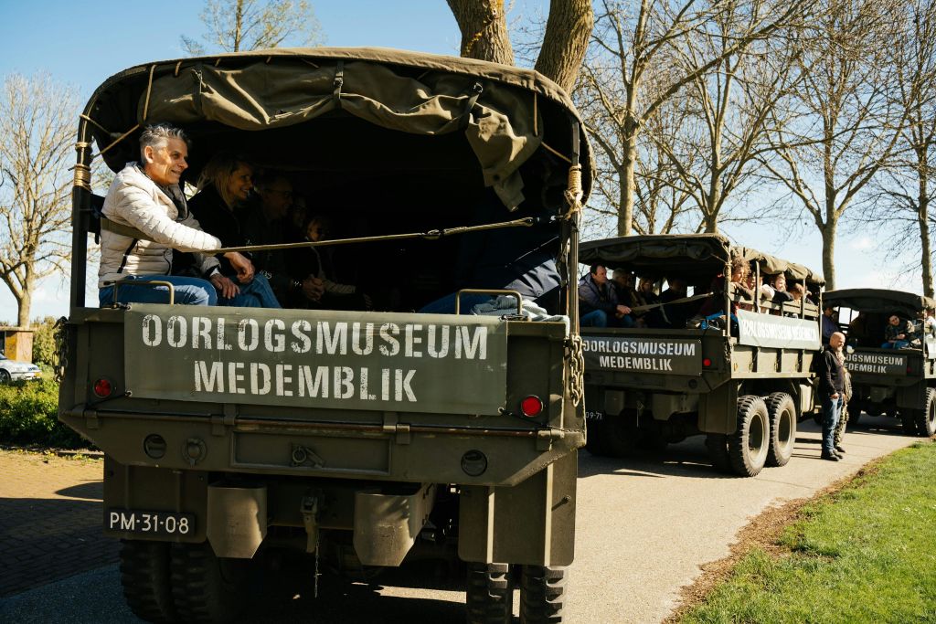 Tourists tour with tour guide through Old Historical Dutch city with WWII Historical Army trucks of a museum