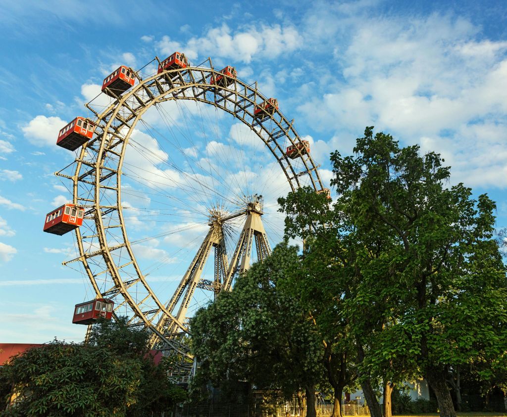 푸르고 부분적으로 흐린 하늘 아래 붉은 통나무집이 있는 대형 관람차는 울창한 녹색 나무로 둘러싸여 있습니다.