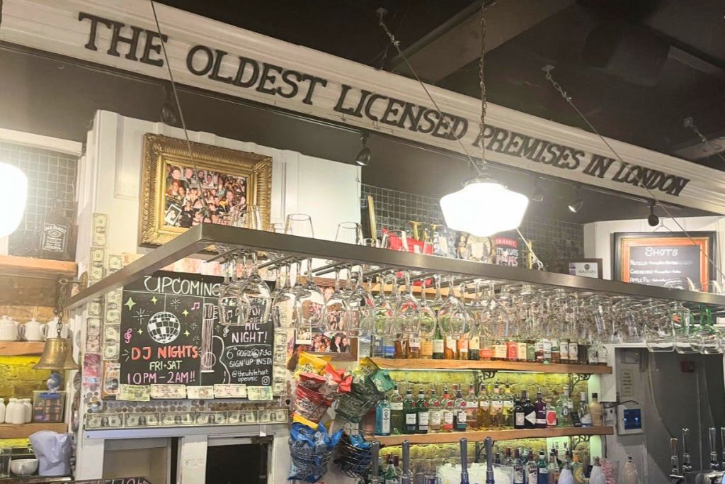 병 선반과 걸이식 안경이 있는 바 내부. 위에 표시된 표지판에는 "가장 오래된 면허를 소지한 건물은..." 이라고 쓰여 있습니다.
