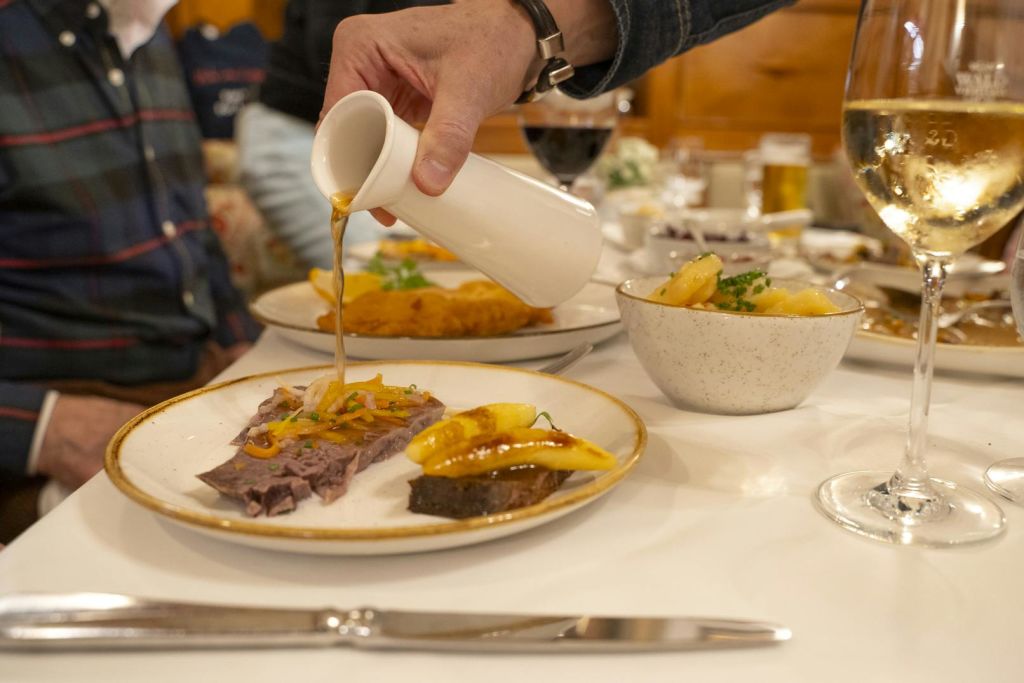 식탁에 놓인 접시에 하얀 주전자의 소스가 담겨 있고, 식기와 음료가 배경으로 놓여 있습니다.