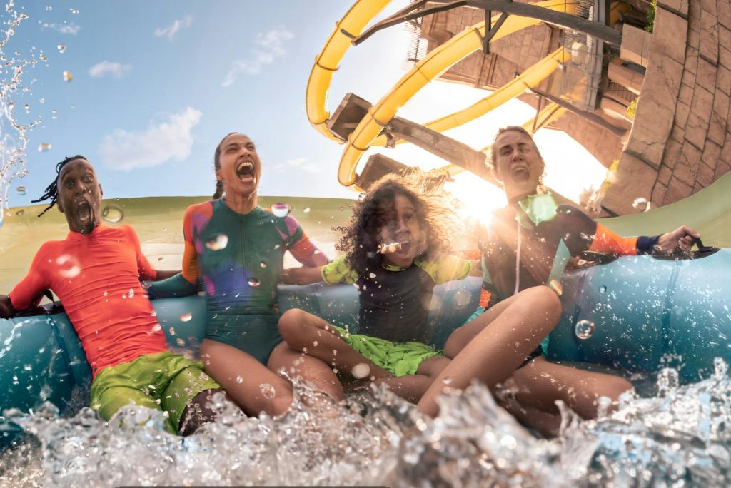 세 사람이 미끄럼틀과 햇빛을 배경으로 물놀이를 즐기며 웃고 있습니다.