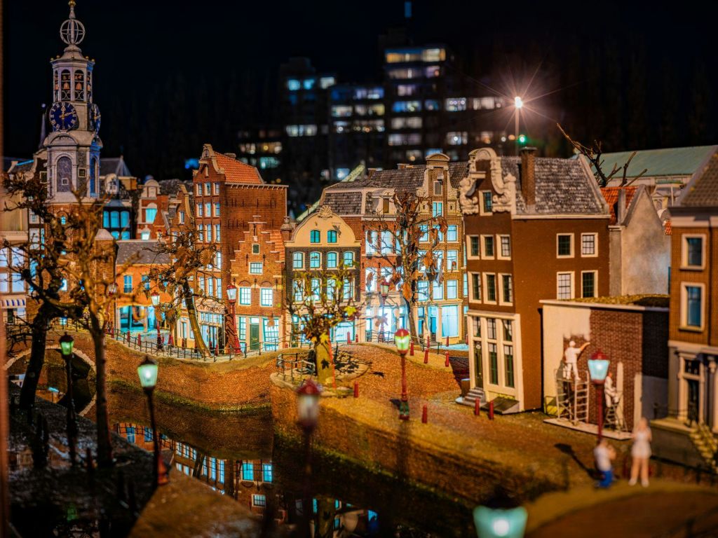 밤하늘을 배경으로 밝고 섬세한 건물, 반사되는 운하, 가로등이 특징인 미니어처 도시 풍경.