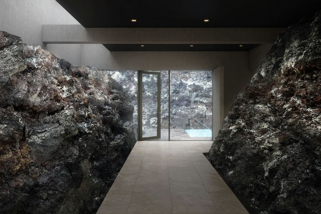 바위 벽, 타일 바닥, 작은 수영장이 있는 야외 공간으로 이어지는 유리문이 있는 내부 복도.