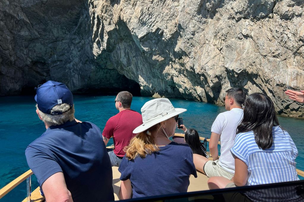 보트 투어를 하는 사람들은 맑고 푸른 물이 흐르는 바위 동굴 입구에 밝은 햇살 아래 다가갑니다.