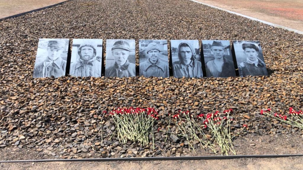 바닥에는 여섯 개의 흑백 초상화가 줄지어 있고, 자갈 침대 앞에는 붉은 꽃이 놓여 있습니다.