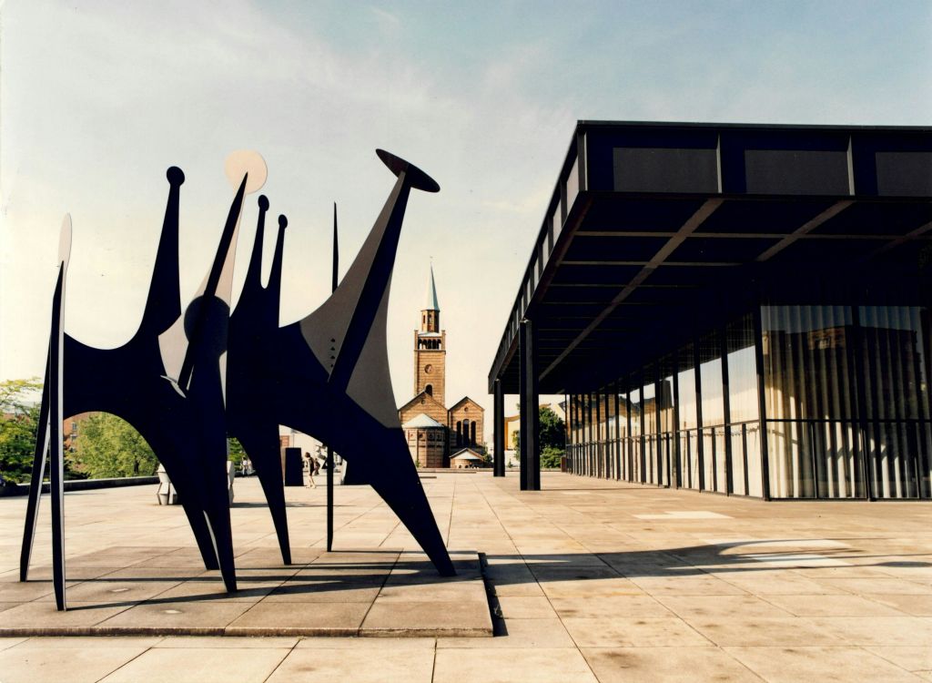 건물 근처 광장에 현대적인 추상 조각품이 세워져 있으며, 교회와 종탑이 배경으로 보입니다.