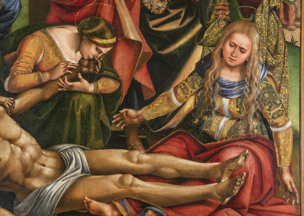 화려한 옷차림과 긴 머리를 한 여성이 화려한 옷을 입은 채 다른 사람들에게 둘러싸인 채 생명이 없는 사람의 팔을 잡고 있습니다.