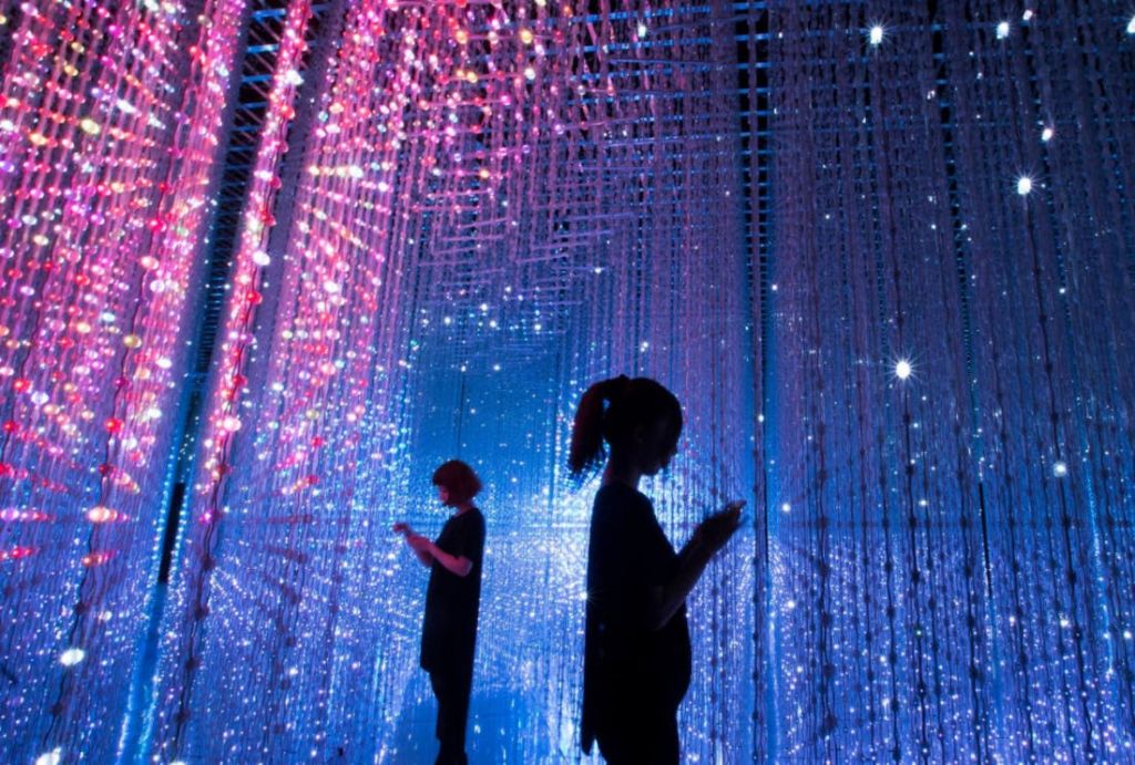 어둡고 몰입감 넘치는 미래 지향적인 공간에서 두 사람이 여러 가지 빛깔의 조명에 매달려 있습니다.