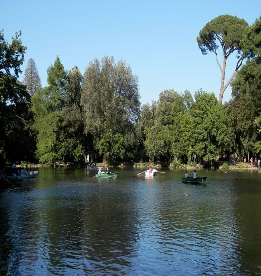 맑고 푸른 하늘 아래 울창한 나무로 둘러싸인 잔잔한 호수에 사람들이 떠다니는 보트.
