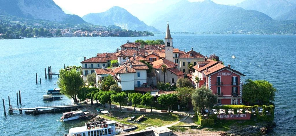 붉은 지붕의 건물, 높은 교회 타워, 산을 배경으로 한 호수가 있는 독특한 마을입니다.