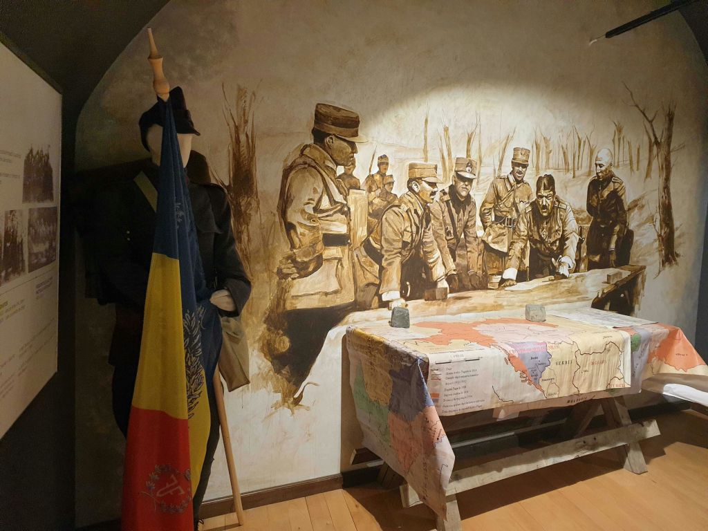 군복을 입은 마네킹이 지도로 덮인 테이블 주위에 모인 군인 벽화 옆에 깃발을 들고 있습니다.