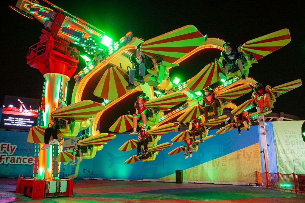 밤에 빨간색과 노란색 캐노피를 들고 밝게 빛나는 놀이공원을 타는 사람들.