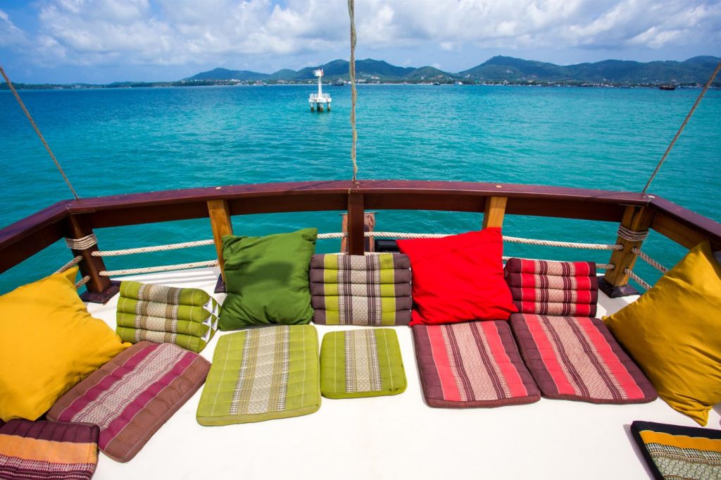 맑고 푸른 물과 부분적으로 흐린 하늘 아래 먼 산이 내려다보이는 보트 데크의 다색 쿠션.
