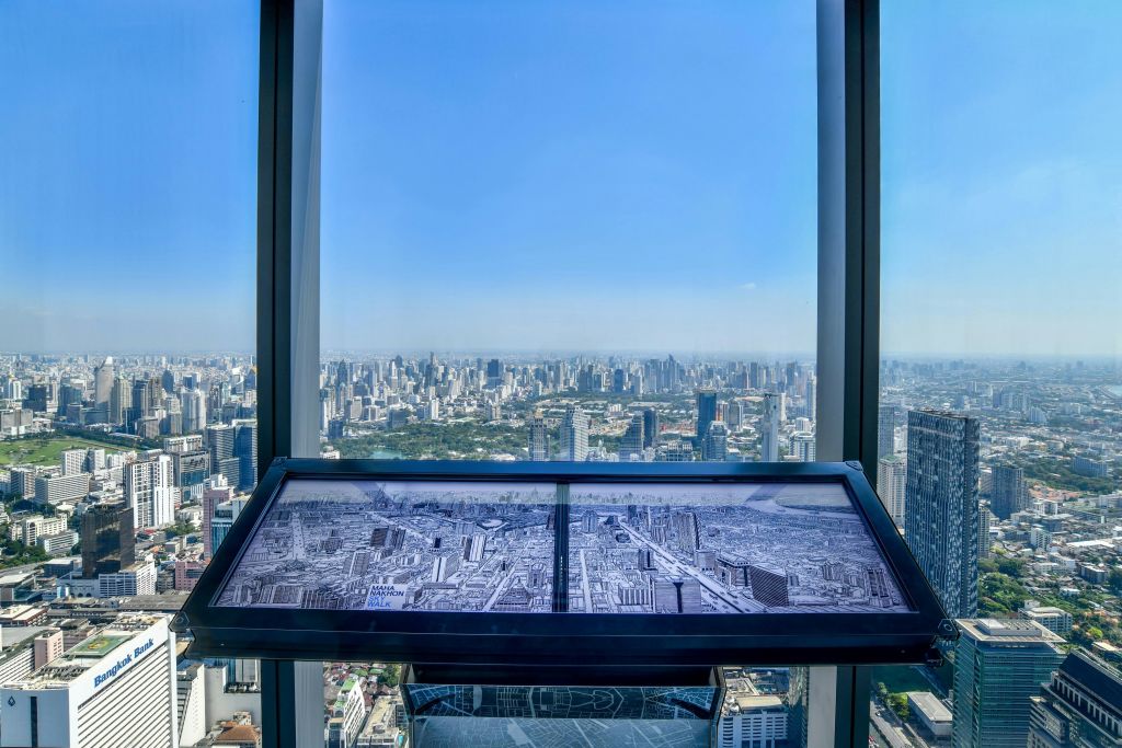 높은 창문으로 내려다보이는 커다란 도시 풍경으로, 전경에 동일한 도시 배치가 표시된 지도가 있습니다.