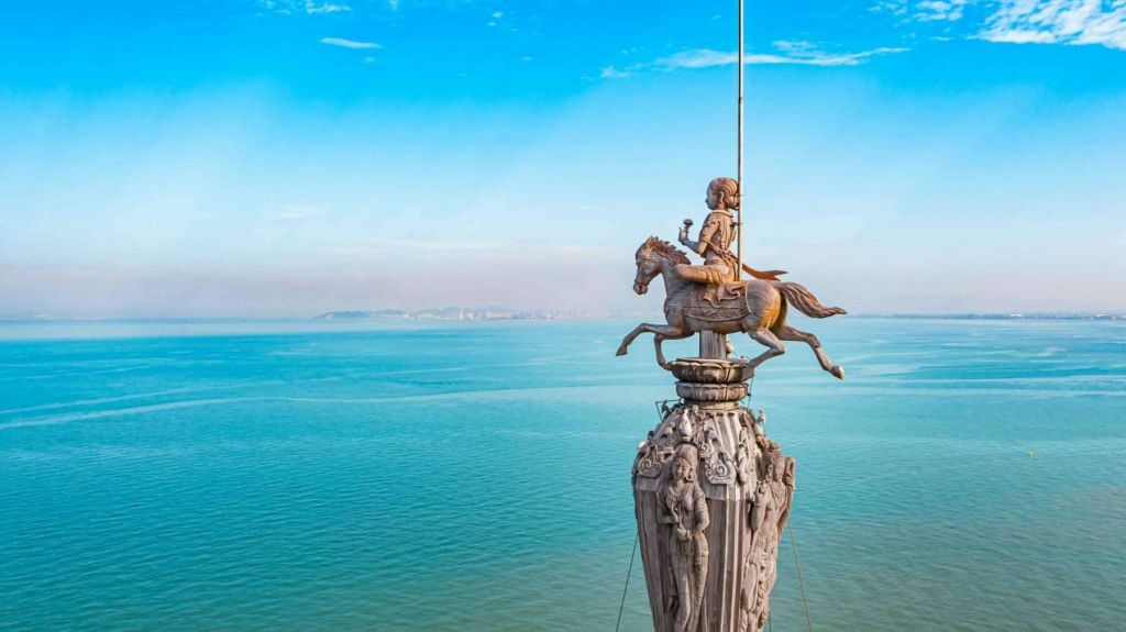 광활한 바다와 맑고 푸른 하늘을 배경으로 기둥 꼭대기에서 말을 타고 있는 사람의 동상.