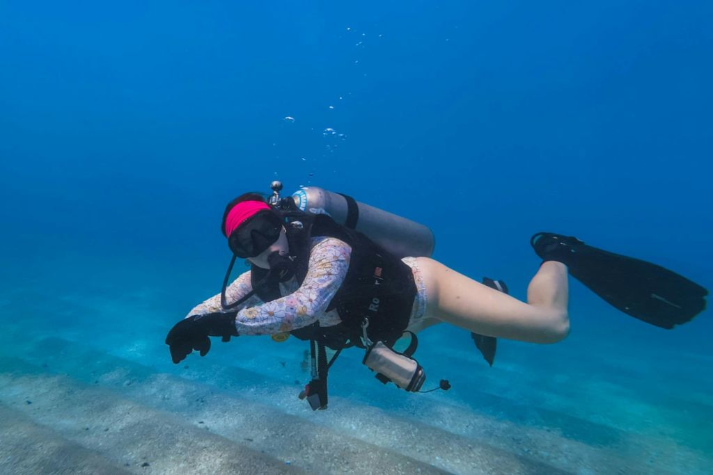 모래 해저 근처에서 빨간 머리띠, 다이빙 장비, 잠수복을 착용한 수중 스쿠버 다이버.