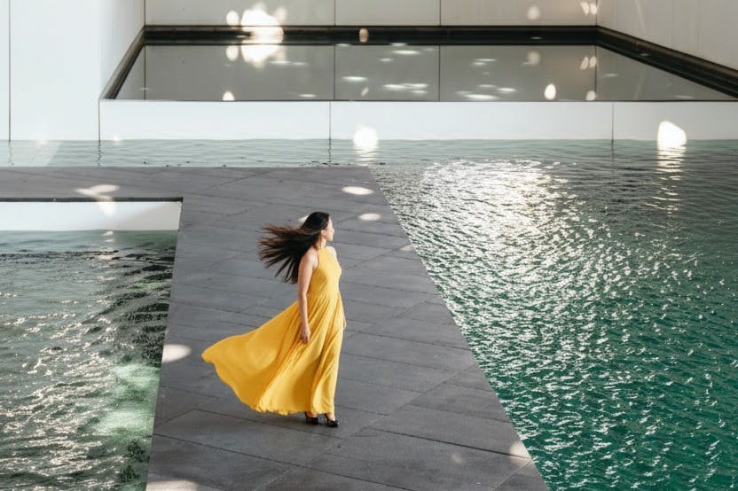 노란색 드레스를 입은 여성이 물웅덩이 근처의 회색 타일 플랫폼에 서 있습니다.