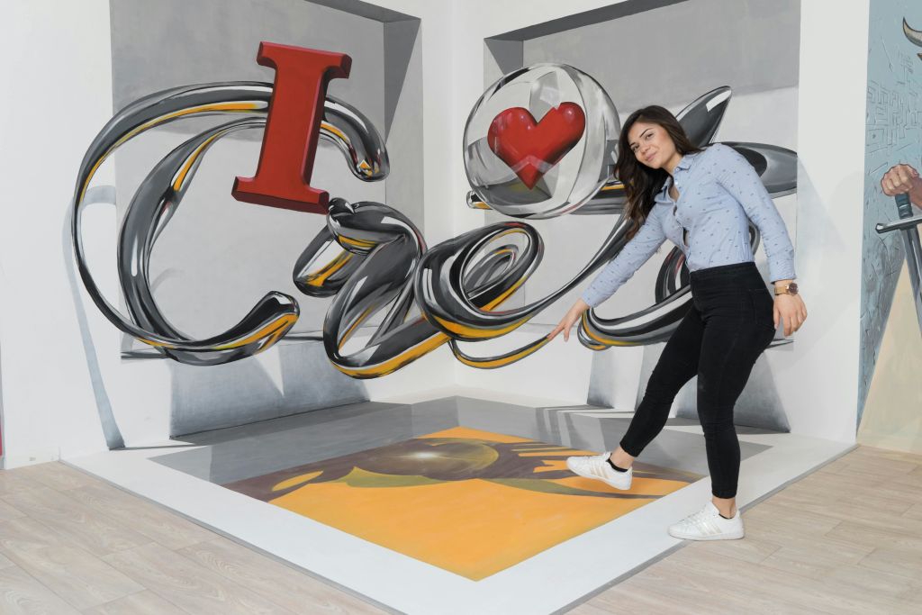 벽에 "I ❤️ Art" 가 그려진 3D 아트 플로어 페인팅에 서 있는 한 여성이 깊이 있는 착시 현상을 연출합니다.