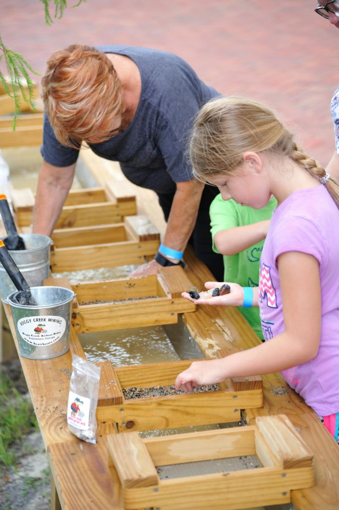 한 소녀가 보석 채굴 활동에 참여하는 동안 손에 든 바위를 살펴봅니다. 성인이 백그라운드에서 도움을 줍니다.