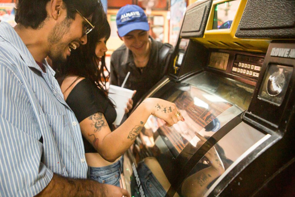 세 사람이 활기찬 분위기에서 주크박스와 상호 작용하며 미소를 짓고 기계에 참여합니다.