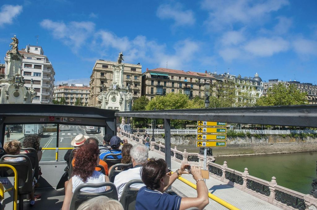 "도노스티아 산 세바스티안 (Donostia San Sebastián)" 이 있는 빨간색 2층 투어 버스가 해안 도로를 따라 운행합니다.