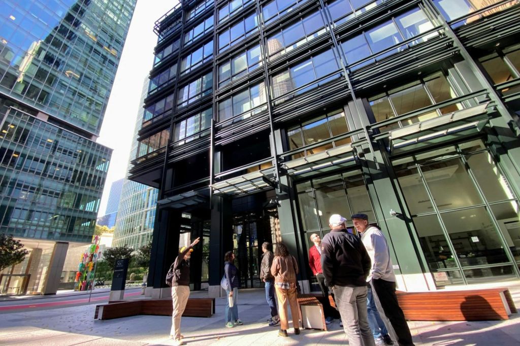 화창한 날에 현대적인 유리 건물 앞에 여러 사람이 서서 이야기를 나누고 있습니다.