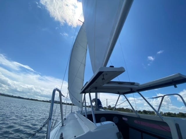 돛을 올리고 잔잔한 물과 부분적으로 흐린 하늘을 배경으로 한 요트 갑판에서 바라보는 풍경.